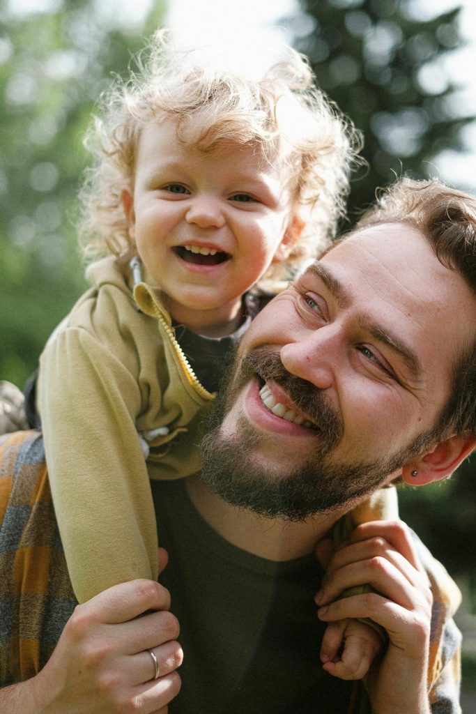 Father and child. Child is stat on father's shoulders. Both are smiling and happy.